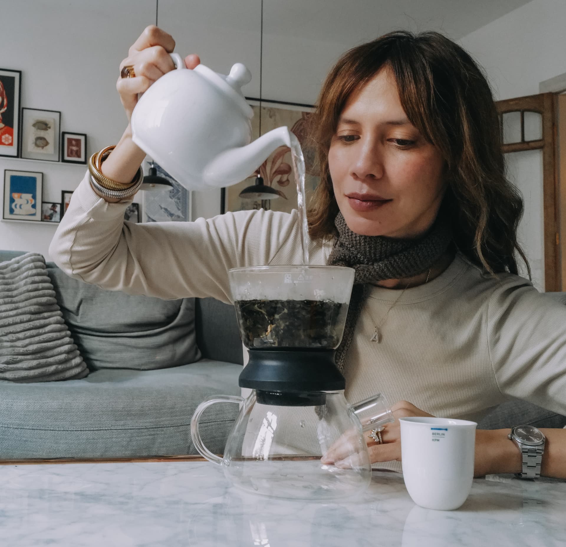 Chele pouring tea from a white teapot into a glass brewer